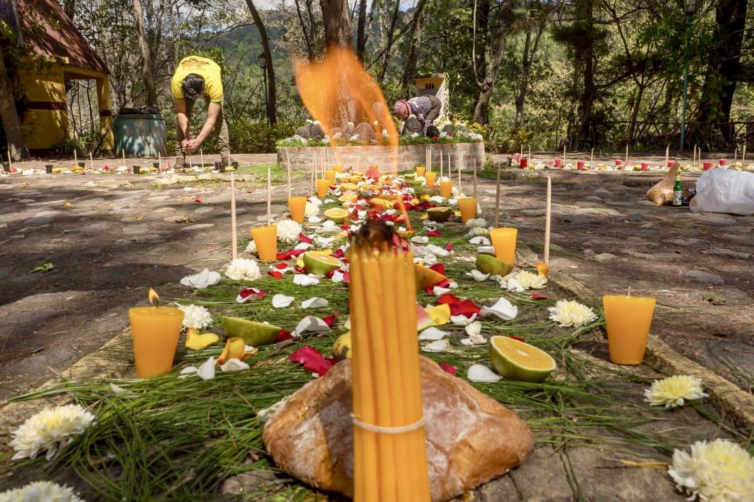 Vorbereitung einer Maya-Zeremonie: Kerzen, Blüten, Früchte und Brot auf Kiefernnadeln, dahinter ein Feuer am Altar