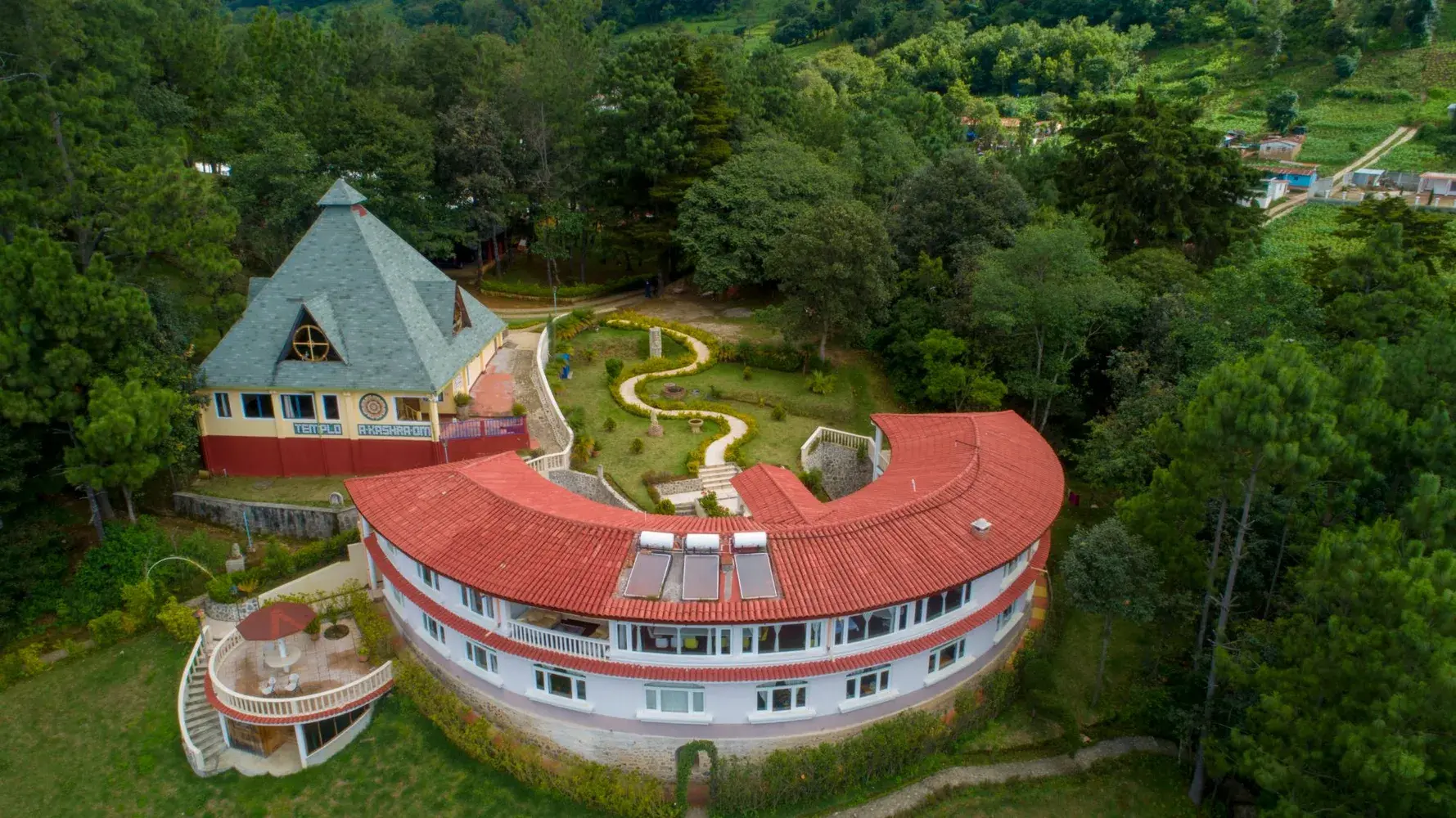 Das Zentrum Paz Mundo von oben, mit dem geschwungenen Hauptbau und dem Tempel im Wald